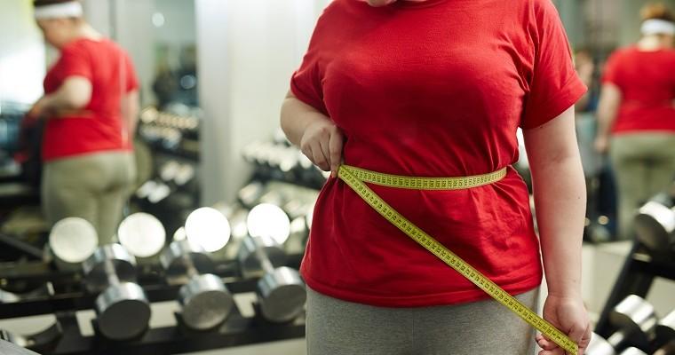 Kobieta z nadwagą mierzy swoją talię na siłowni