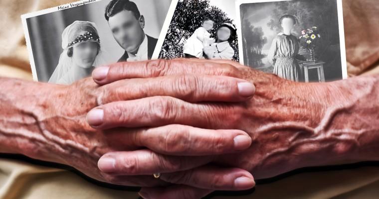 Ręce starszej osoby ściskają stare fotografie. Wszystkie twarze sfotografowanych osób są rozmazane