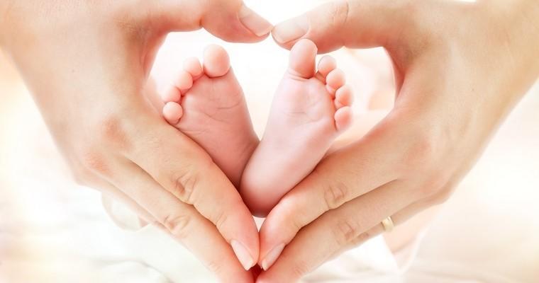 Matka trzyma stopy niemowlaka układając wokół nich kształt serca