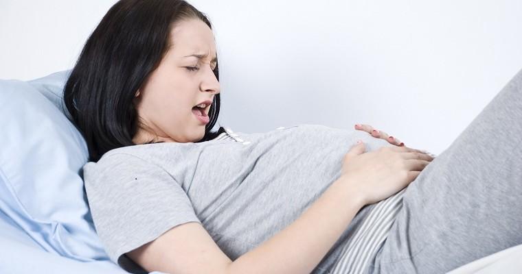 Kobieta w ciąży leży na łóżku i trzyma sie za brzuch