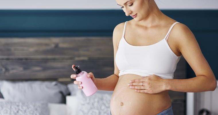 Kobieta w zaawansowanej ciąży smaruje swój brzuch kremem. 