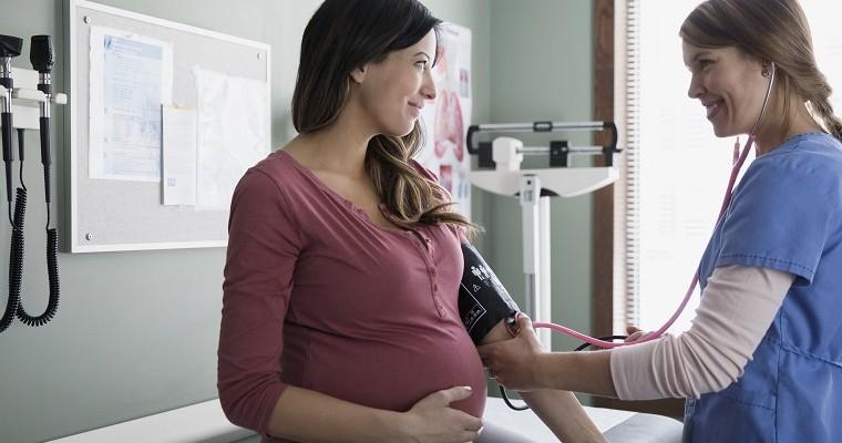 Kobieta w ciąży siedzi na kozetce. Pielęgniarka mierzy ciężarnej ciśnienie.