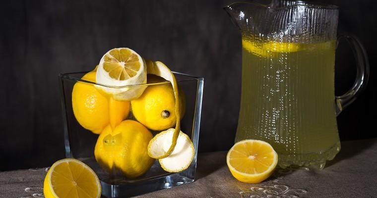 Woda z cytryną, z sokiem z cytryny w karafce, obok, w szklanej misce obok. Sok z cytryny działa korzystnie na organizm ponieważ zawiera składniki odżywcze.