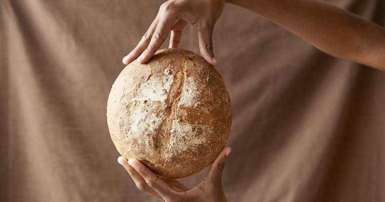 Chleb, okrągły bochenek chleba trzymany w dłoniach.