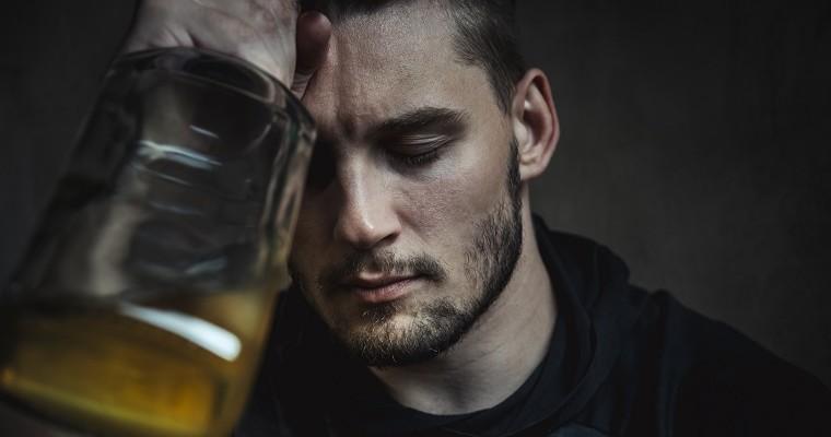 Pijany młody mężczyzna trzyma w dłoni butelkę z alkoholem.  