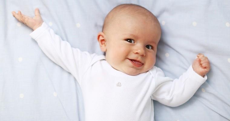 uśmiechnięty niemowlak leżący na błękitnej pościeli