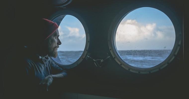 Mężczyzna patrzy przez okno na statku i patrzy na morze.