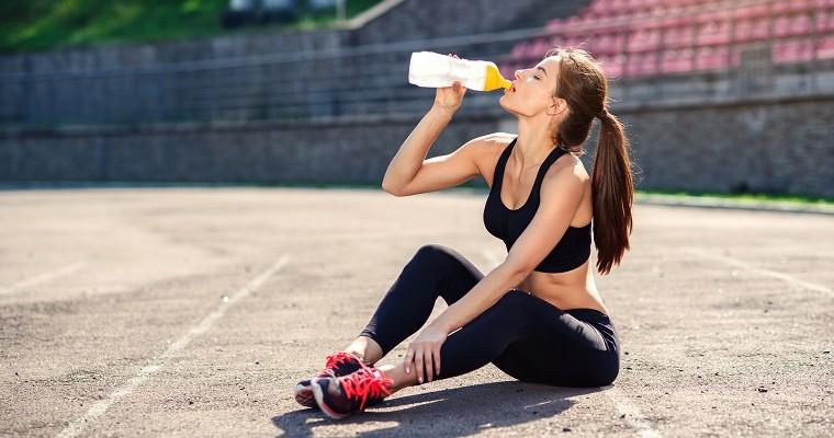 Młoda kobieta siedzi po treningu i pije wode 