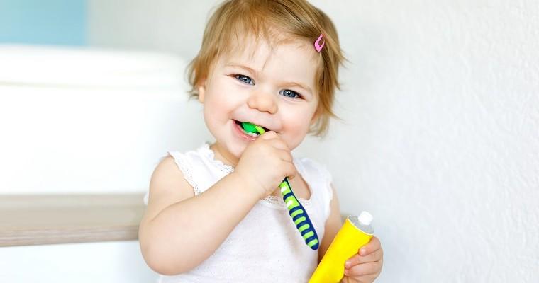 Małe dziecko myje zęby szczoteczka w reku trzyma tubkę pasty. 