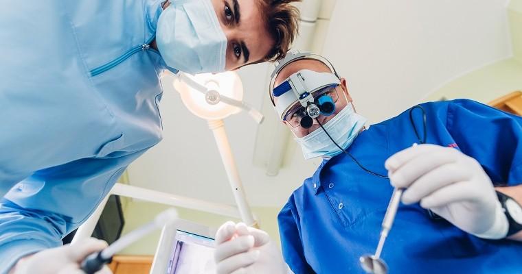 Dentysta i osoba asystująca ubrani na niebiesko z opaską ochronna na ustach.