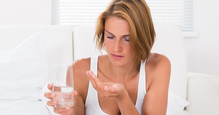 Kobieta w białym podkoszulku łyka tabletki wczesnoporonne