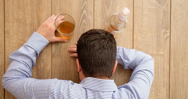 Pijany mężczyzna położony na stole, obok butelka i szklanka z alkoholem