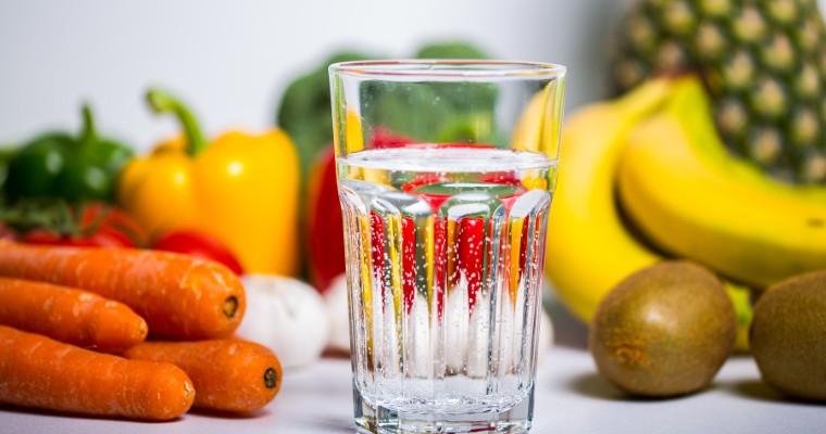 Zdjęcie szklanki z wodą oraz owocami i warzywami w tle