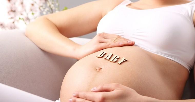 Kobieta w ciąży trzymająca się za brzuch, na którym widać napis baby