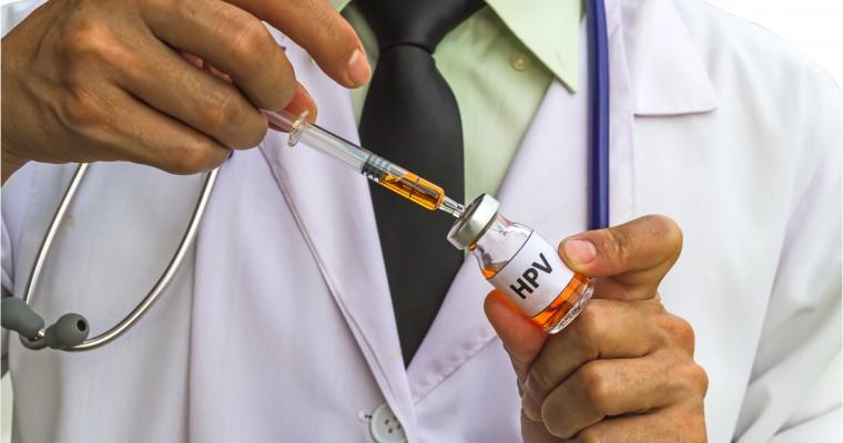 Lekarz napełnia strzykawkę lekiem. Na butelce widnieje napis "HPV"